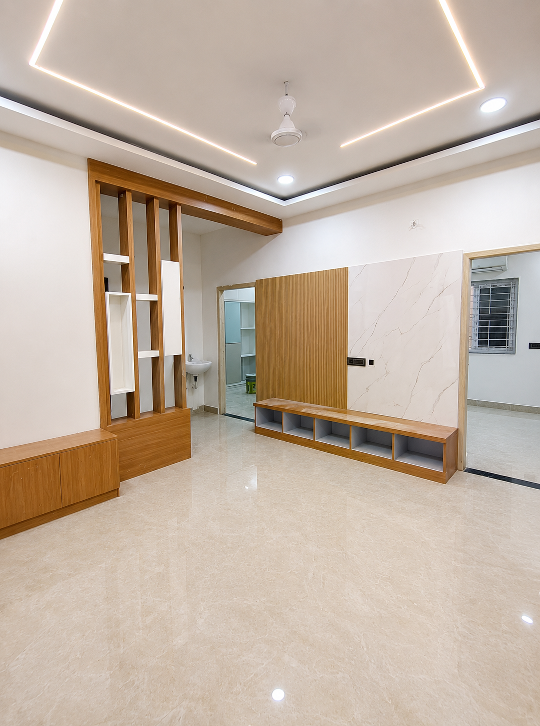 Modern TV unit, wooden TV panel, TV wall design, wooden partition, decorative wooden partition, living room partition, wooden display shelves, built-in TV cabinet, TV storage unit, wall-mounted TV unit, modern false ceiling, LED false ceiling, cove lighting, ceiling strip lights, designer ceiling, recessed ceiling lights, ceiling fan, glossy marble flooring, marble floor living room, spacious floor area, open-plan living room, modern interior design, contemporary home interior, wooden interior work, wood finish furniture, wall panel design, fluted wall panel, marble wall panel, decorative wall panel, entertainment unit, TV console cabinet, open storage shelves, built-in storage, living room storage cabinet, modern electrical switch panel, clean wall design, bright interior space, well-lit living room, spacious home entrance, interior doorway, wooden door design, modern door frame, attached wash basin, wall-mounted wash basin, compact wash area, premium interior finishes, polished flooring, apartment interior design, modern rental home interior, furnished rental living room, spacious rental apartment.